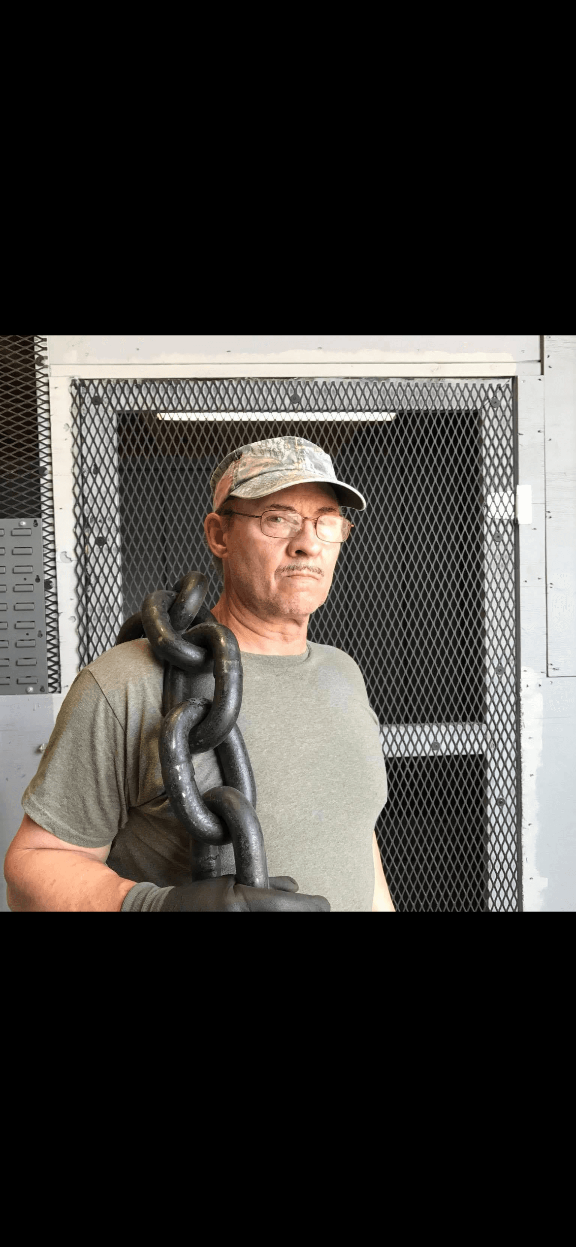 Man with glasses and camouflage hat carries a heavy black chain over his shoulder.