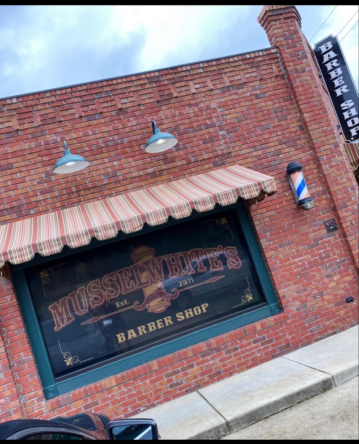 Musselwhite's Barber Shop storefront with a brick facade, striped awning, and a classic barber pole.